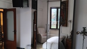 Een slaapkamer met een bed, een kledingkast, een stoel, een televisie en een raam.
