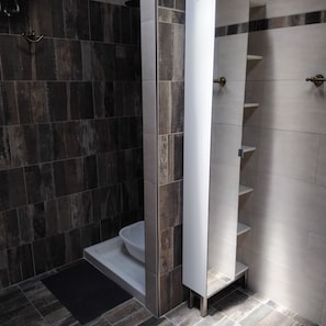 A modern bathroom with dark tiles, a white toilet, and a built-in shower with a white shelf.