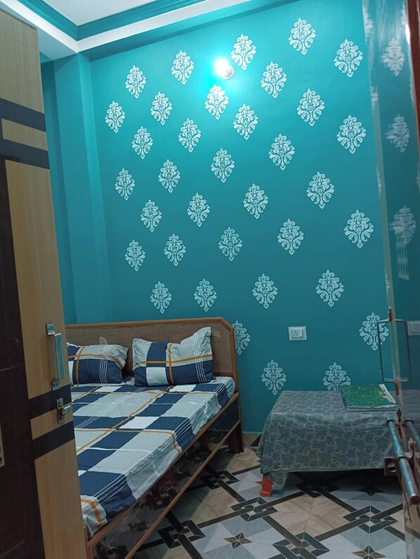 A room with a bed, a small table, and a wall with decorative patterns. - Guest House nr. Subhasnagar Lakshman (Varanasi)