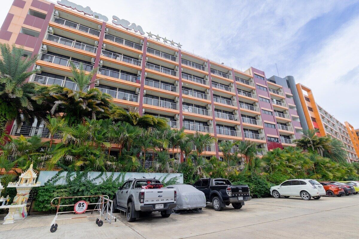 Un hotel de varios pisos con balcones, un estacionamiento y palmeras.