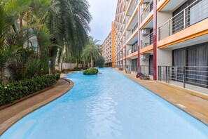 Ein Pool mit gewölbter Kante, umgeben von Grünflächen und einem mehrstöckigen Gebäude mit Balkonen.