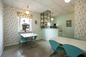 Een kamer met een witte tafel, teal stoelen, een zwart rek en een raam met uitzicht.