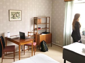 Habitación de hotel con escritorio de madera, una computadora portátil, estantería, cama y ventana con cortinas.