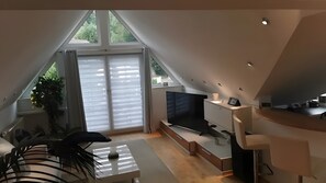 Un dormitorio tipo loft moderno con un tragaluz grande, un televisor de pantalla plana, un escritorio y una zona de comedor.
