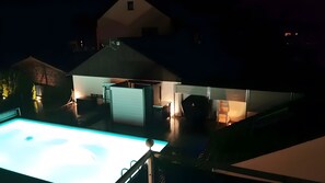 A swimming pool with a covered area, a patio, and a house in the background.