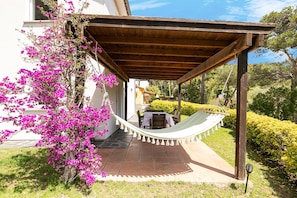 Un área de estar al aire libre techada con una hamaca, una mesa de patio y sillas.