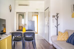 Un espace de vie compact comprenant un coin repas, un canapé agrémenté de coussins à motifs et un porte-manteau.