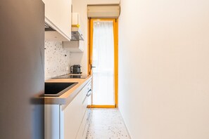 Eine schmale Küche mit einem schwarzen Spülbecken, weißen Schränken und einem Fenster mit einer gelben Tür.