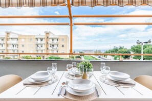 Une table à manger dressée avec des assiettes, des verres et des couverts, donnant sur un quartier résidentiel avec des immeubles et une route.