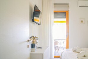 Ein Hotelzimmer mit Bett, Schreibtisch mit Vase, Fenster mit Vorhängen und Blick ins Freie.