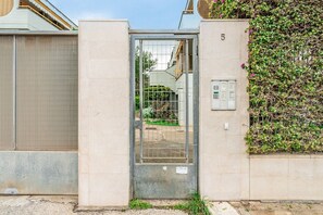Ein verschlossener Eingangsbereich mit einer Metalldürre, einer Betonmauer mit der Nummer 5 und einer Mauer, die von Kletterpflanzen überwuchert ist.