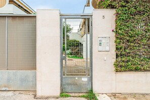 Une entrée fermée par un portail en métal, une porte, un panneau indiquant le numéro « 5 » et un mur muni d’un système de sécurité.