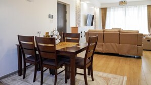 A dining area with a wooden table and chairs, a sofa set, and a television in the background. - Cozy 2bedroom apartment in beautiful Nairobi, wit gym,swimming pool & City views (Kangundo)