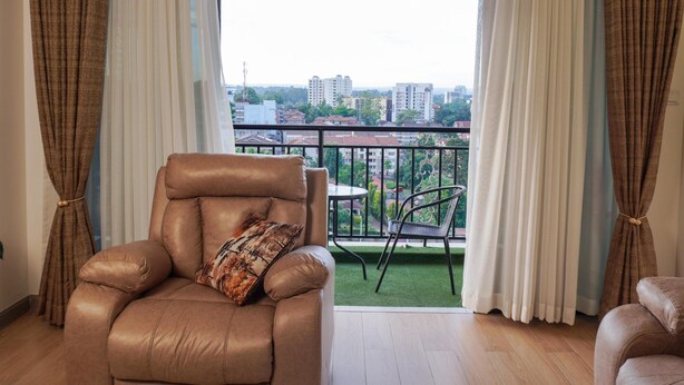 A living room with a leather sofa, a patterned throw pillow, a dining table with chairs, and a view of a cityscape through large windows. - Cozy 2bedroom apartment in beautiful Nairobi, wit gym,swimming pool & City views (Kangundo)