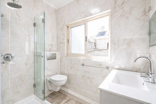 A modern bathroom with a glass shower enclosure, a toilet, and a sink with a mirror. - MAMAD Duplex & Panoramic Terrace near Beach | FeelHome (Tel Aviv - Jaffa)