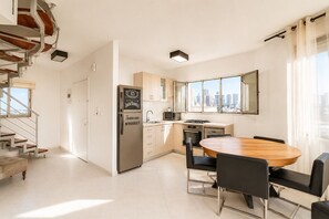 A modern kitchen with a built-in refrigerator, a dining table with chairs, and a city view through large windows. - MAMAD Duplex & Panoramic Terrace near Beach | FeelHome (Tel Aviv - Jaffa)