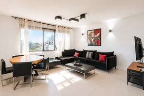 A modern living room with a black sofa, a round wooden table, and a coffee table. - MAMAD Duplex & Panoramic Terrace near Beach | FeelHome (Tel Aviv - Jaffa)