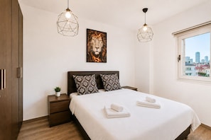 A bedroom with a bed, two bedside tables, a nightstand, a window with a city view, and two hanging lights. - MAMAD Duplex & Panoramic Terrace near Beach | FeelHome (Tel Aviv - Jaffa)