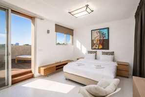 A bedroom with a bed, a chair, a desk, a window, and a painting. - MAMAD Duplex & Panoramic Terrace near Beach | FeelHome (Tel Aviv - Jaffa)