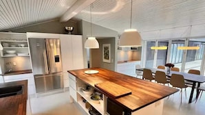 A modern kitchen with a wooden island, stainless steel appliances, pendant lighting, and a dining area with chairs and a table. - 4 Star Holiday Home in Nykobing Sj (Nykobing Sjaelland)
