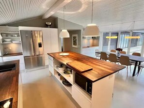 Eine moderne Küche mit einer Holztischinsel, Edelstahlgeräten, Pendelleuchten und einem Essbereich mit Stühlen und einem Tisch.