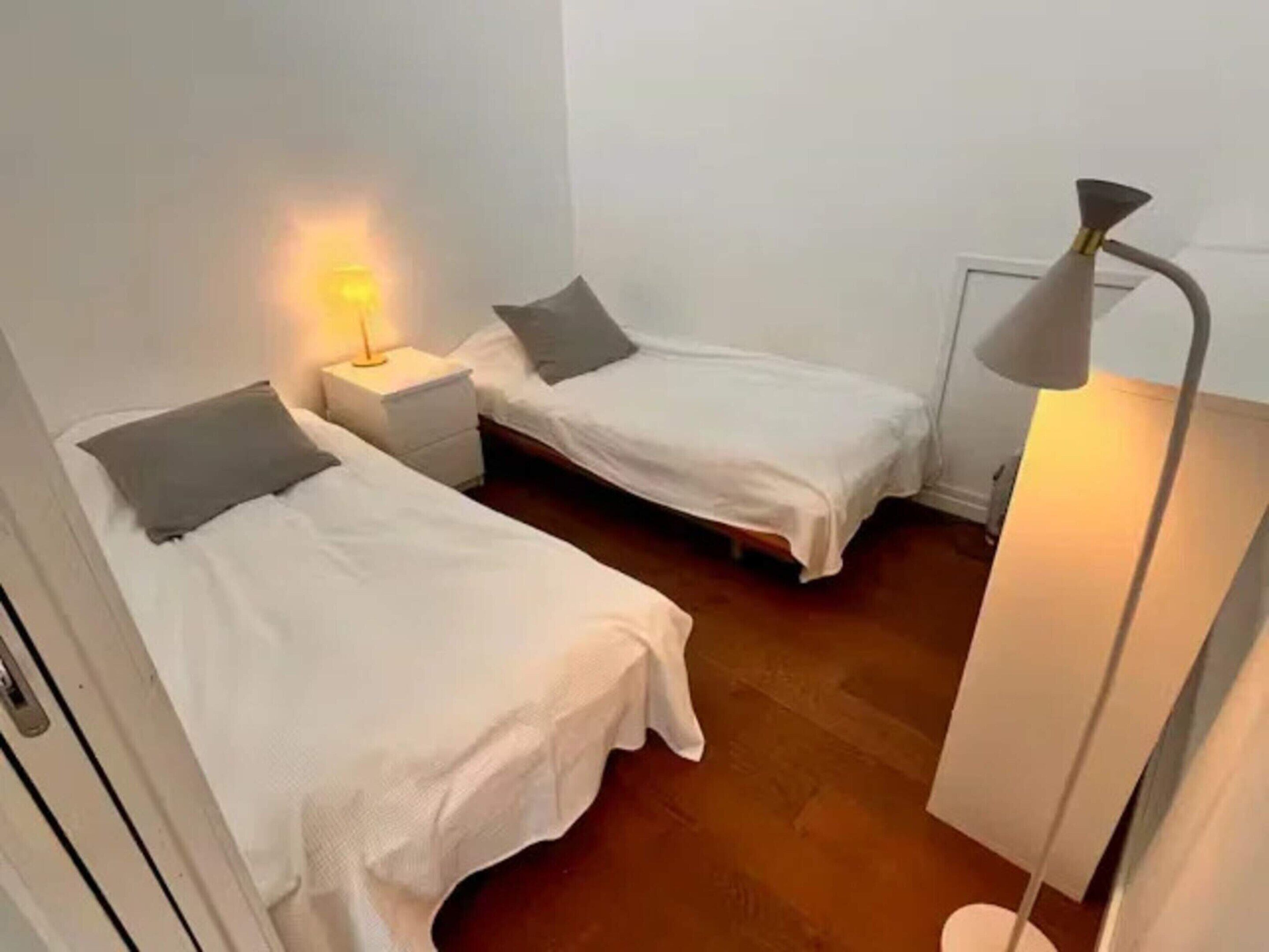 Een kamer met twee eenpersoonsbedden, een nachtkastje met een lamp en een radiator.