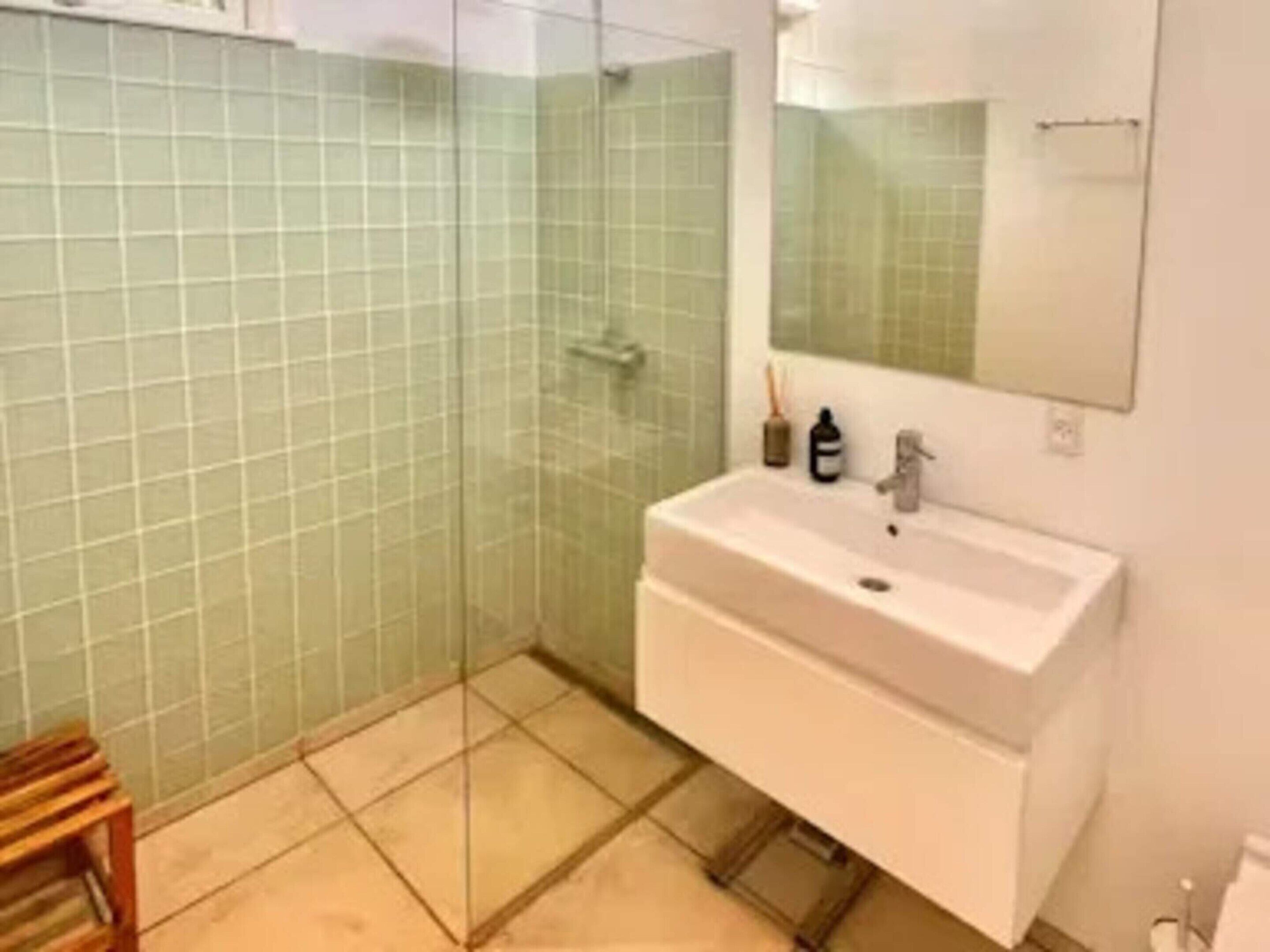 A bathroom with a glass shower enclosure, a white sink, and a mirror.