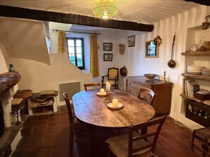 Une salle à manger rustique avec une table ronde en bois, des chaises, un lustre et une fenêtre avec des rideaux.