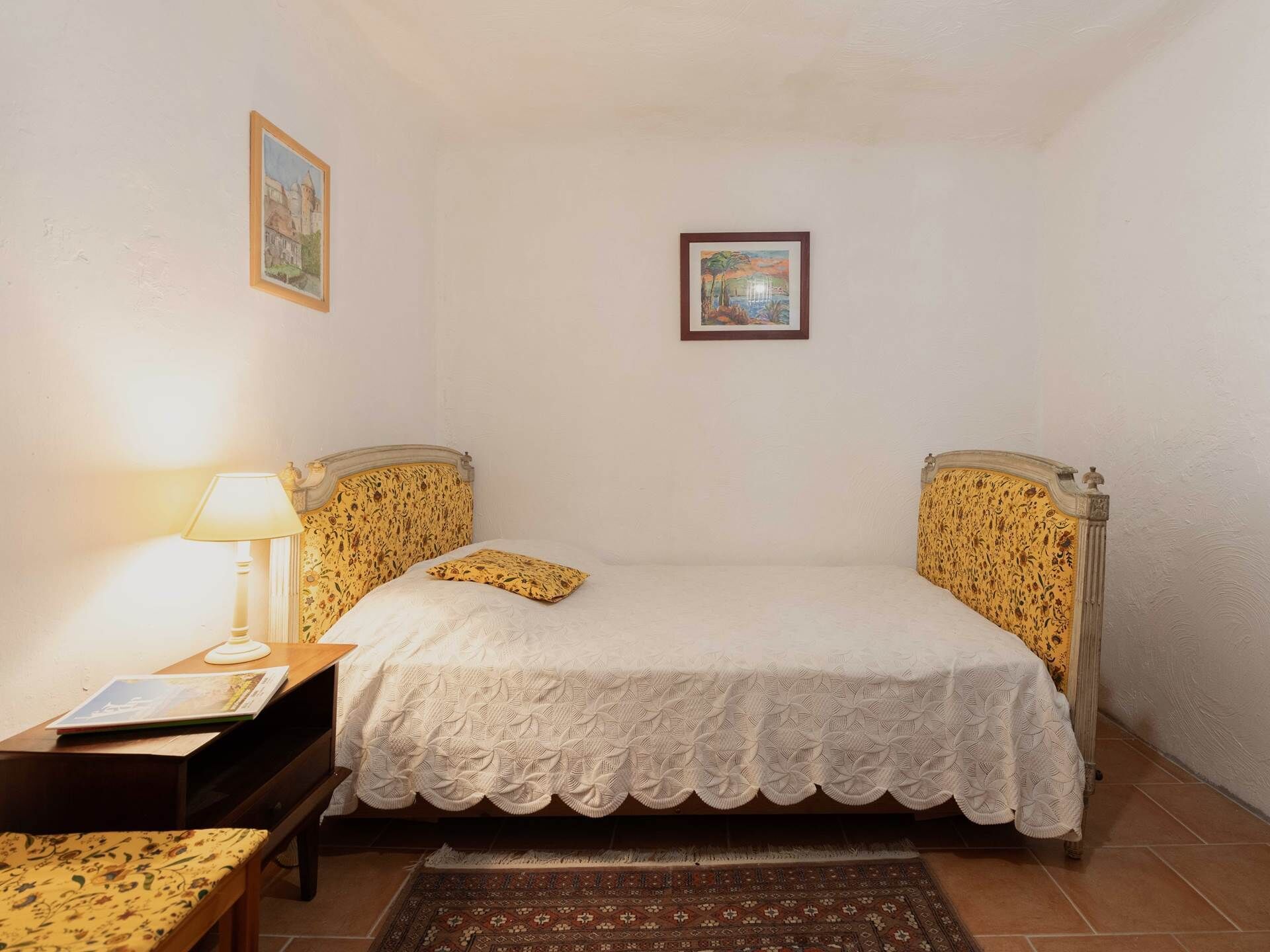 Una camera da letto con un letto, due cuscini, un comodino con una lampada e un tappeto.