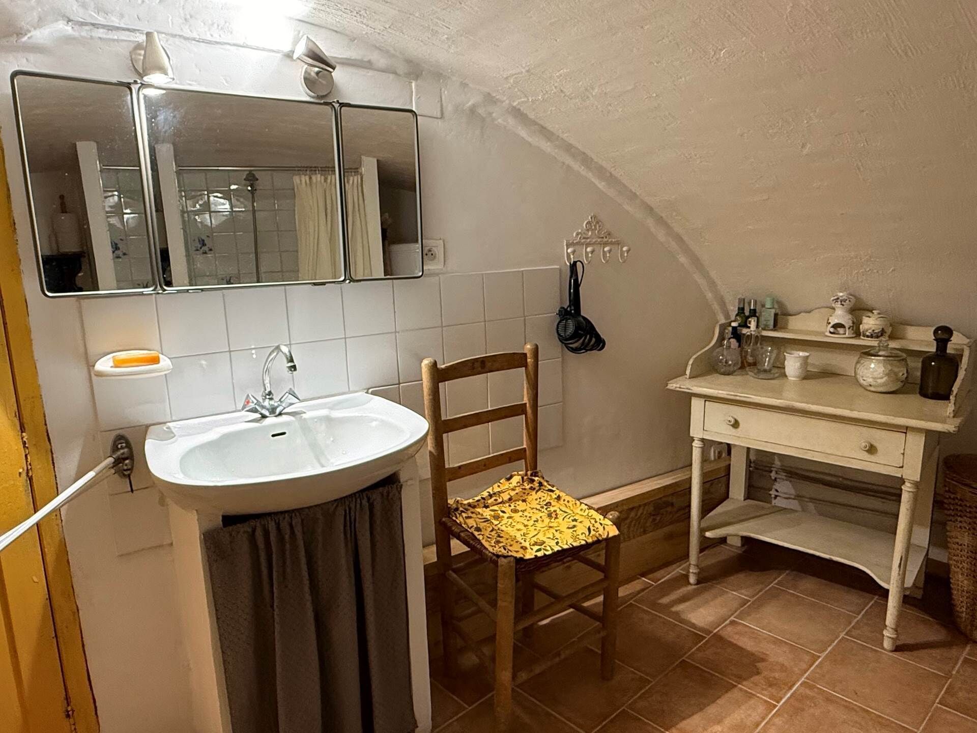 A bathroom with a sink, mirror, towel rack, chair, and a vanity with toiletries.