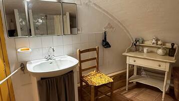 A bathroom with a sink, mirror, towel rack, chair, and a vanity with toiletries.