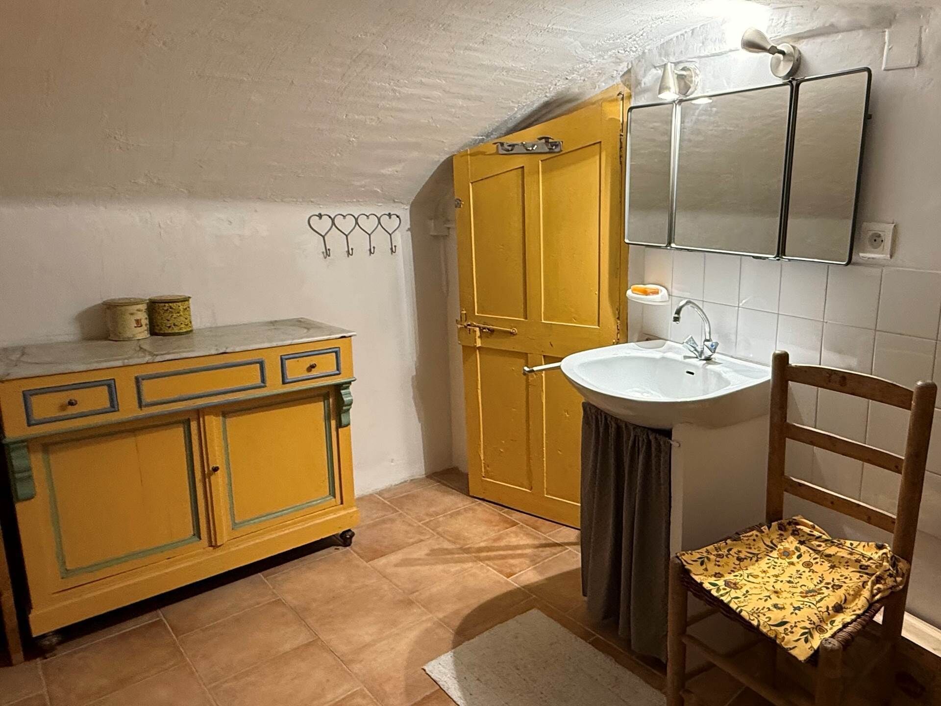 Een badkamer met een geel kastje, een wit wastafel en een houten stoel.