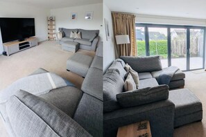 En moderne stue med en grå hjørnesofa, et fladskærms-tv, et træunderholdningsmøbel og en stor skydedør, der fører ud til en have.