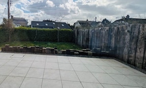 Ein gepflasterter Innenhof mit Holzzaun, einer Hecke und einem Gebäude mit Satteldach im Hintergrund.