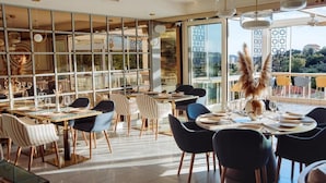 A modern dining area with multiple tables and chairs, large windows, and a view of the outdoors. - Status M Apartments 152 (Becici)