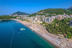 An aerial view of a coastal city with a beach, buildings, and a mountainous backdrop. - Status M Apartments 152 (Becici)