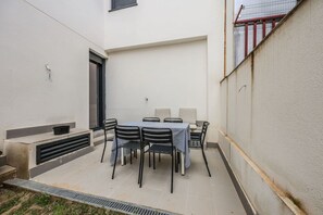 Een terras met een tafel, stoelen, een klein raam en een deur.
