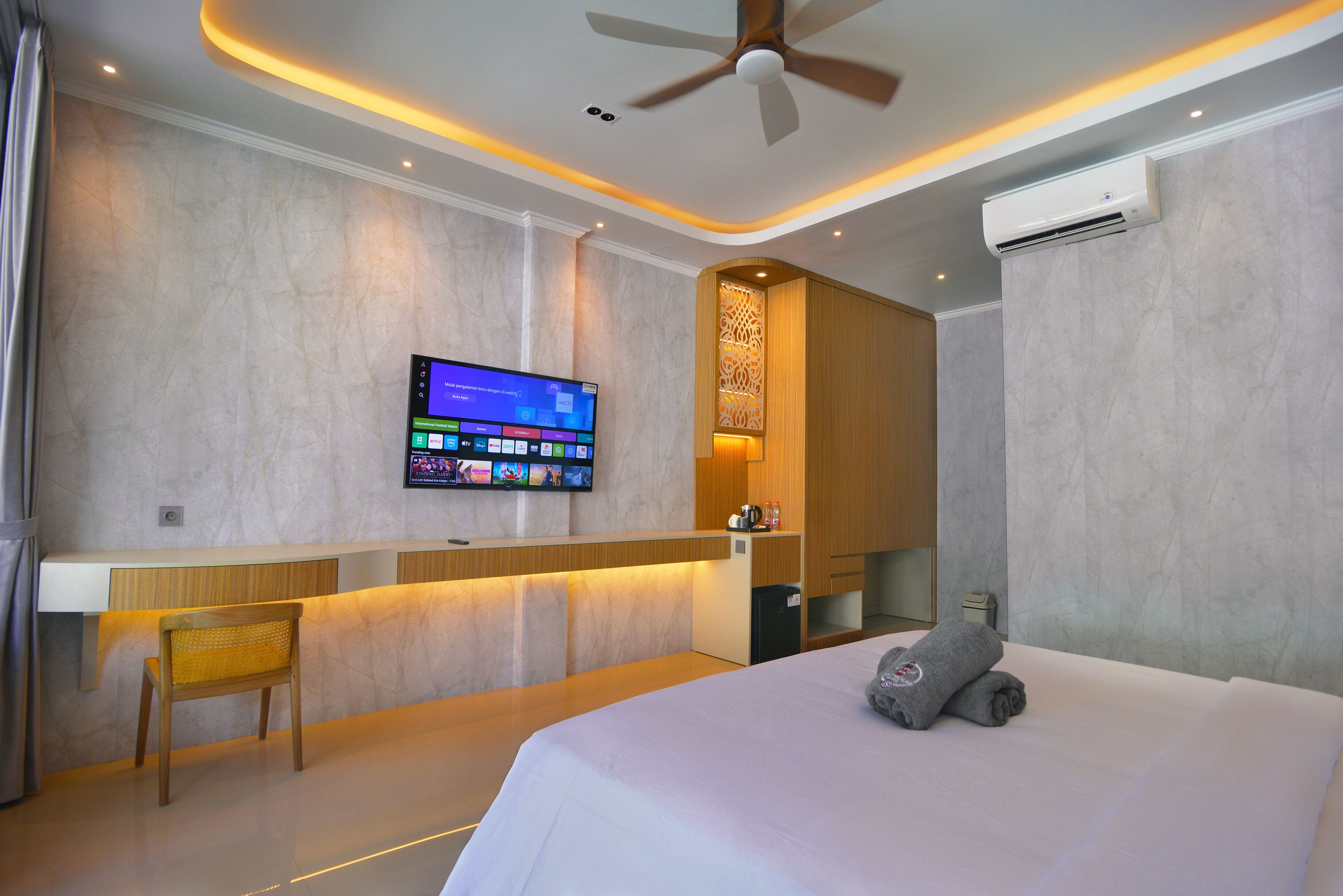 A hotel room with a bed, a desk, a television mounted on the wall, and a ceiling fan.