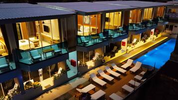 A modern hotel with multiple balconies, a swimming pool, and outdoor seating areas.