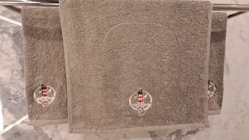 Three towels with a lighthouse logo on a metal towel rack against a marble wall.