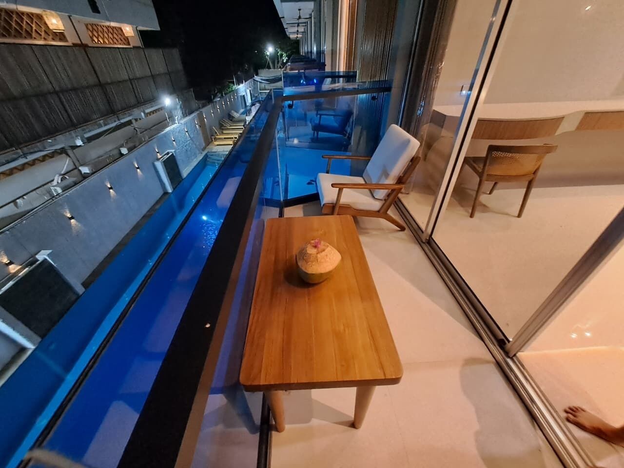 A modern indoor pool area with a wooden table and chairs, a small decorative item on the table, and a glass railing overlooking the pool.