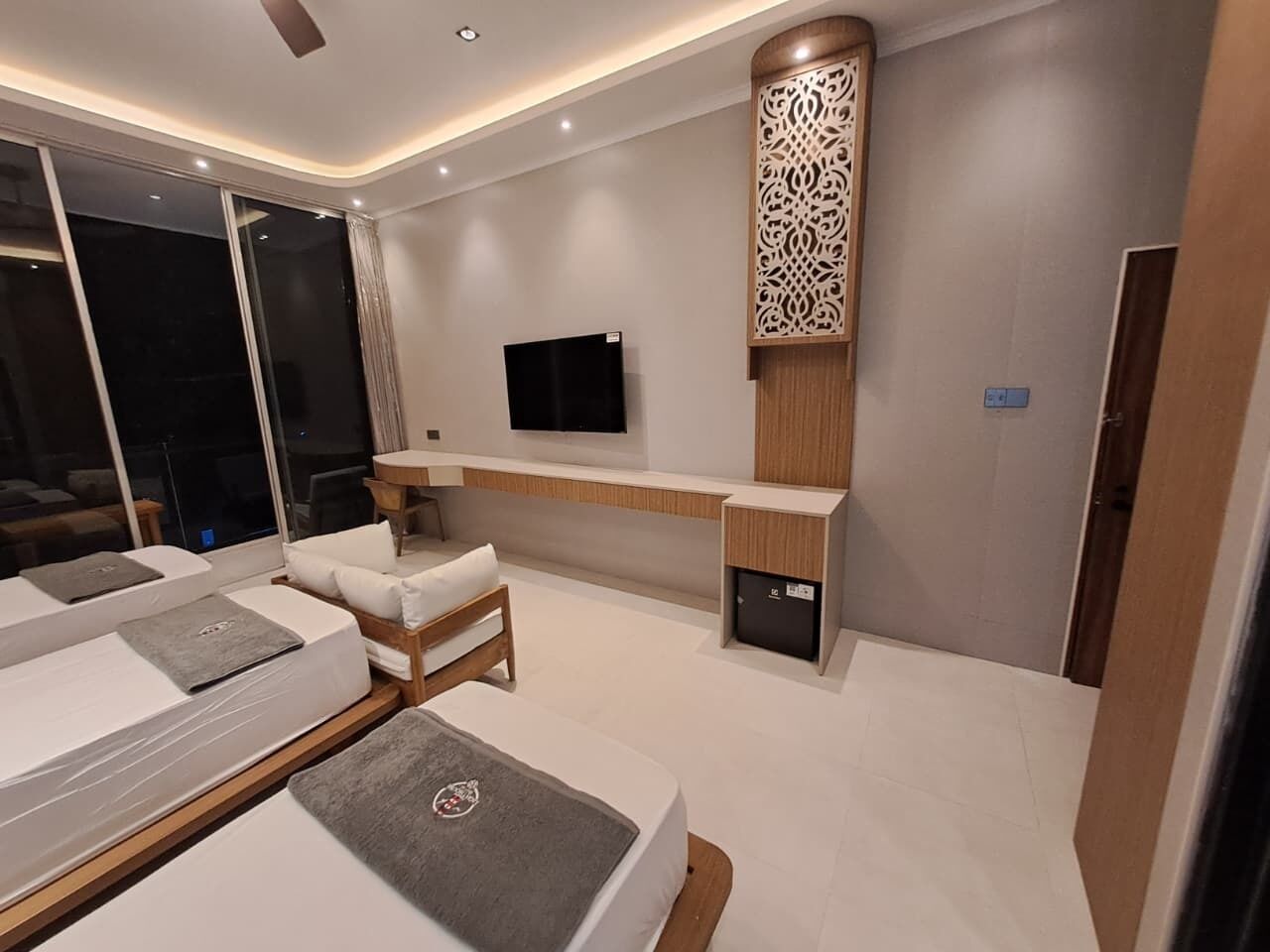 A modern hotel room with a large bed, a sofa, a TV, and a decorative wall panel.