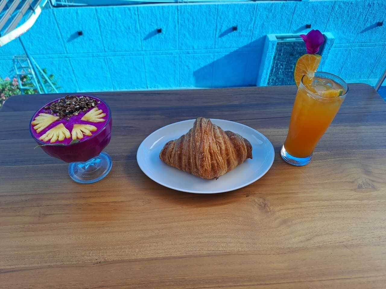 A wooden table with a dessert bowl, a croissant, and a glass of orange juice.