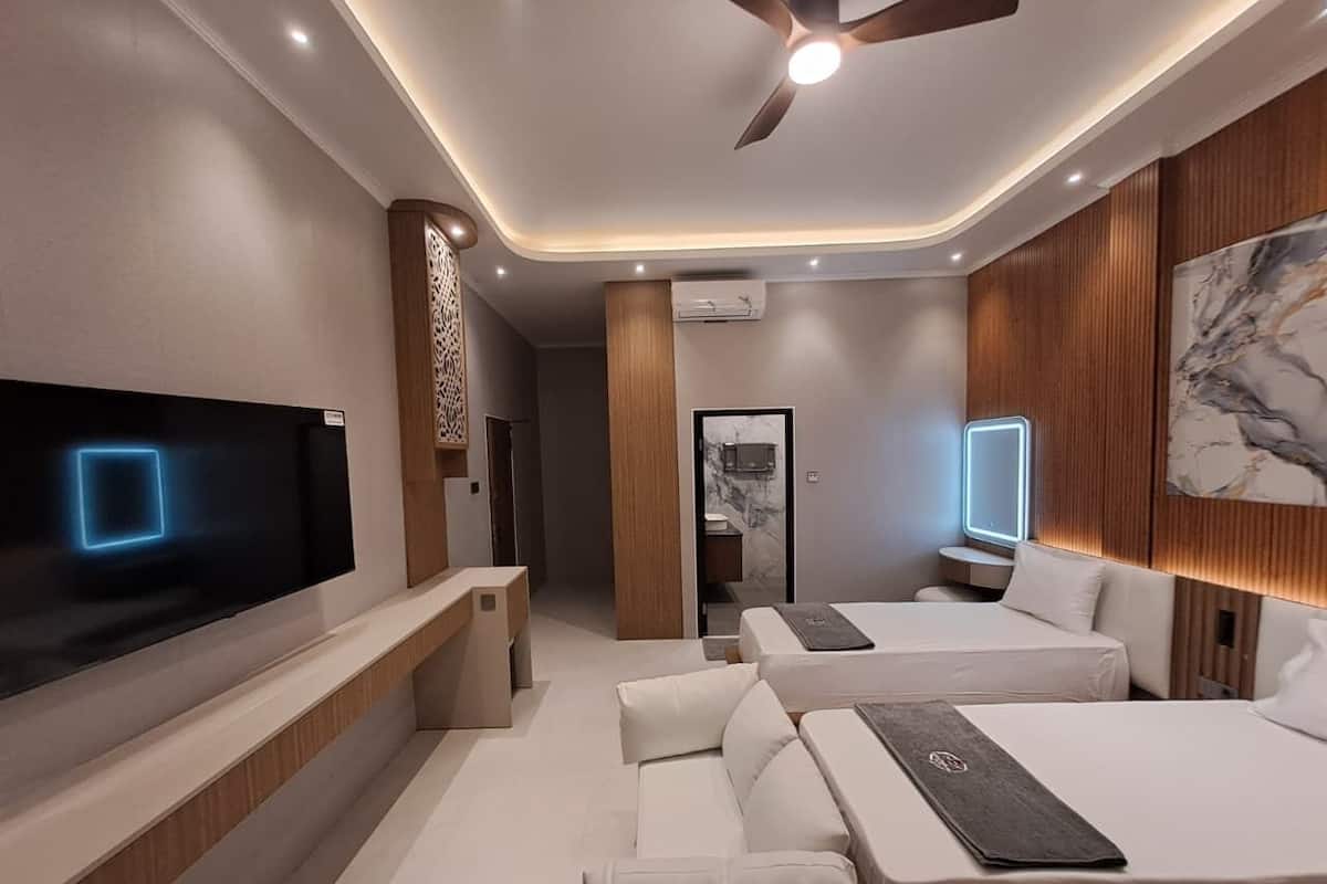 A modern hotel room with a flat-screen TV, two beds, a seating area, and a ceiling fan.