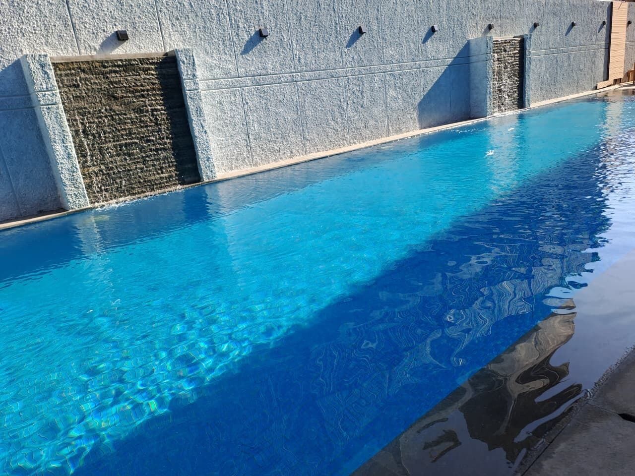A swimming pool with clear blue water, a stone wall, and a small waterfall feature.