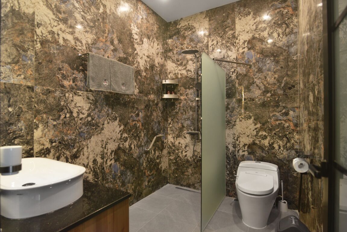 Un baño con pared de mármol, ducha, inodoro y lavamanos.