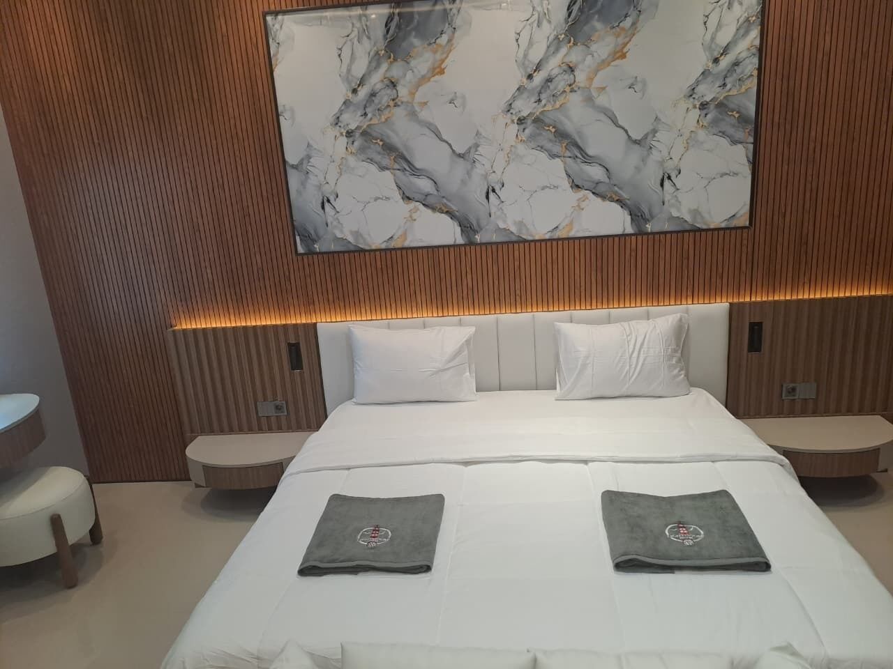 A modern hotel room with a large bed, two bedside tables, a marble wall art piece, and a wooden panel wall.