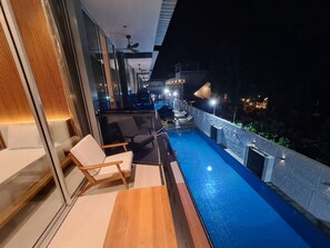 Un balcón moderno con piscina, mobiliario y vistas nocturnas de la ciudad.