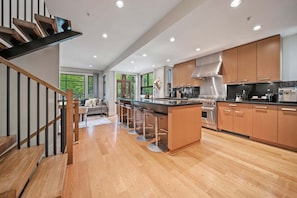 Eine moderne Küche mit Holzausbau, einer zentralen Kochinsel inklusive Barhocker und einer Treppe mit schwarzer Geländer.