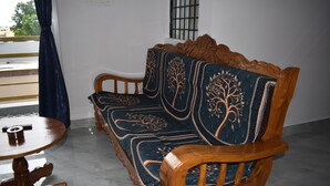 Un sofá de madera con diseños intrincados, una mesa redonda de madera y una ventana con barrotes.
